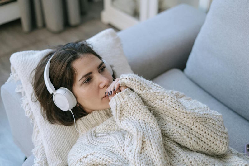 Une femme allongée sur un canapé, l’air pensif et distant, écoute de la musique en silence, signe d’un détachement émotionnel dans la relation.